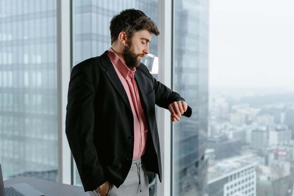 A professional in a suit stands thoughtfully looking out a large office window at a city skyline, representing a high-stakes investment decision.