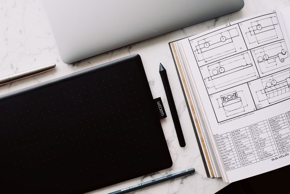 A minimalist overhead view of architectural blueprints and a tablet on a clean desk, representing the strategic analysis and restructuring of commission models.